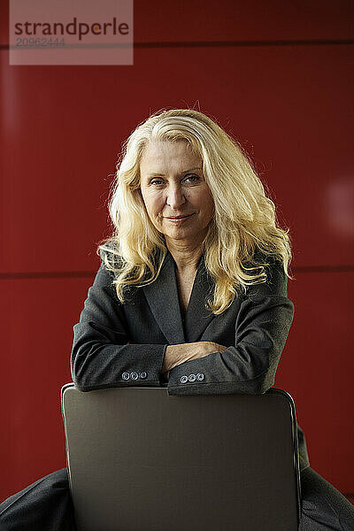 Blond businesswoman sitting on chair near red wall