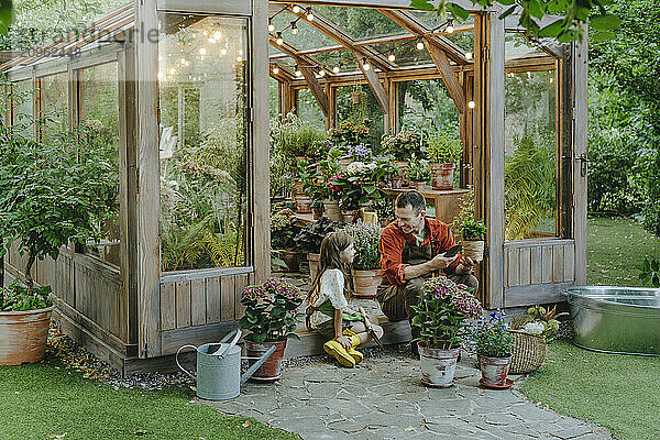 Father and daughter sitting at doorway of greenhouse in back yard