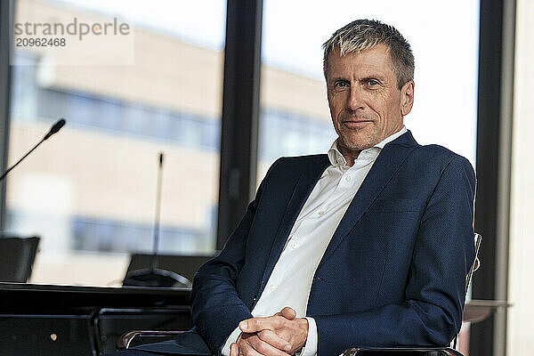 Confident businessman with hands clasped sitting on chair at office