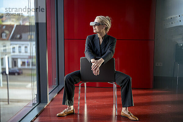 Senior businesswoman wearing virtual reality headset and sitting on chair