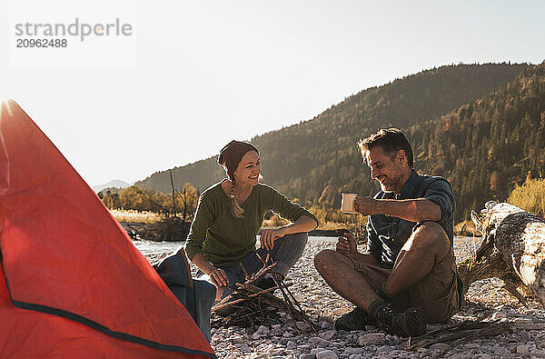 Mature woman with boyfriend holding mug sitting near riverside