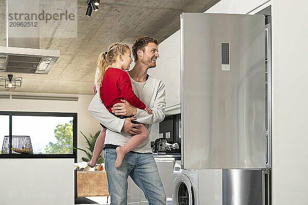 Happy man and daughter looking in refrigerator at home