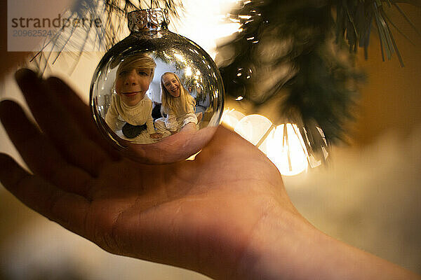 Reflection of brother and sister on Christmas ornament