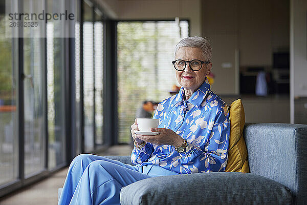 Senior woman sitting on couch at home with cup of coffee