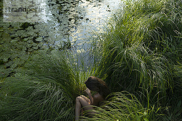 Woman sitting on green grass near pond