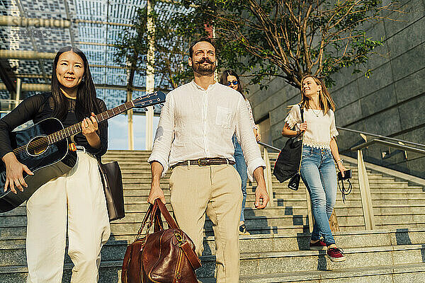 Smiling woman holding guitar with friends moving down on staircase