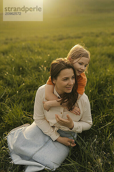 Daughter hugging mother sitting in meadow