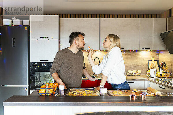 Beautiful woman feeding man in kitchen at home