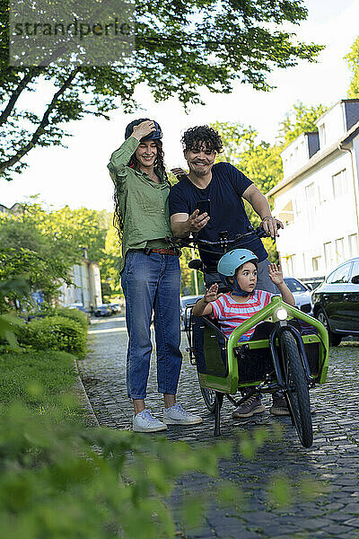 Father and mother with daughter sitting in cargo bike on cobbled street