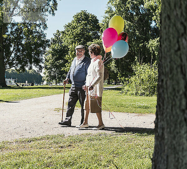 Happy senior couple walking with balloons in park