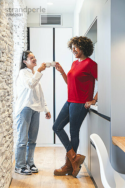 Cheerful friends doing celebratory toast with coffee cups in hotel room