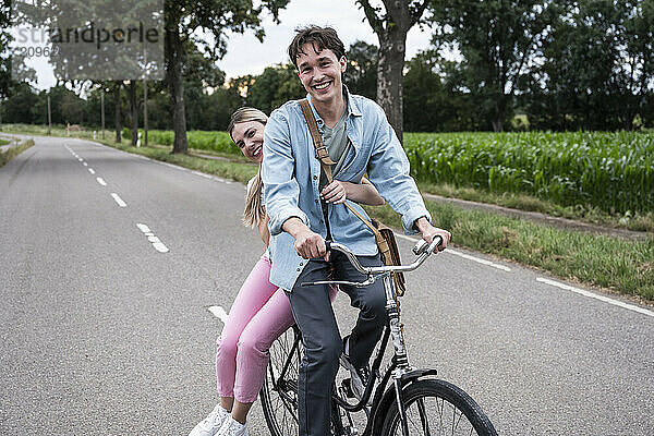 Happy woman sitting behind boyfriend riding bicycle on road