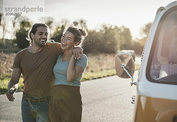 Cheerful couple walking near van on road