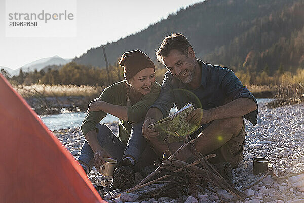 Smiling couple reading map and sitting at riverside