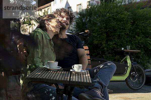 Happy woman leaning on man sitting on bench at street