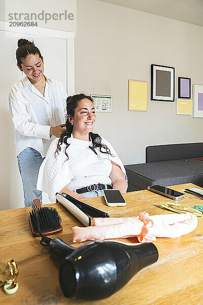 Smiling woman curling hair of friend at home