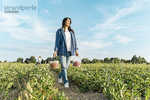 Happy woman walking with bucket full of strawberries in field