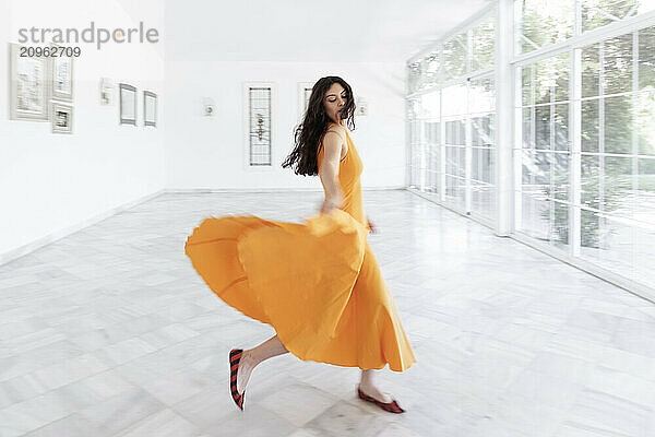 Beautiful woman in orange dress dancing in villa