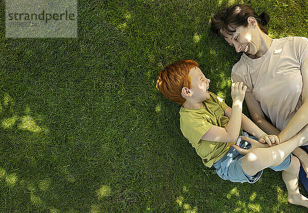 Playful mother and son lying on grass in garden