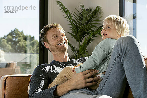 Happy son with father sitting on sofa at home