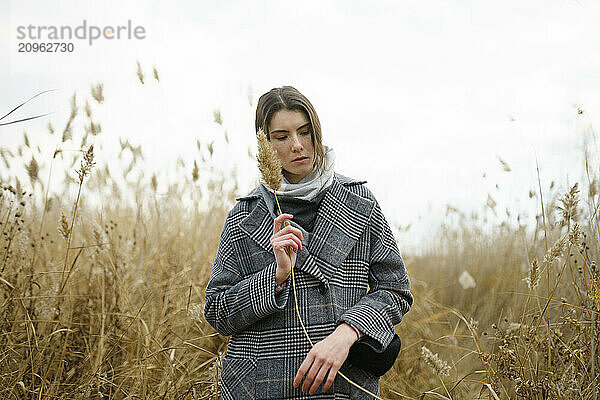 Woman in trench coat holding pampas amidst reeds