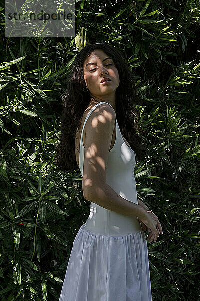 Beautiful woman with eyes closed standing in shade near plants