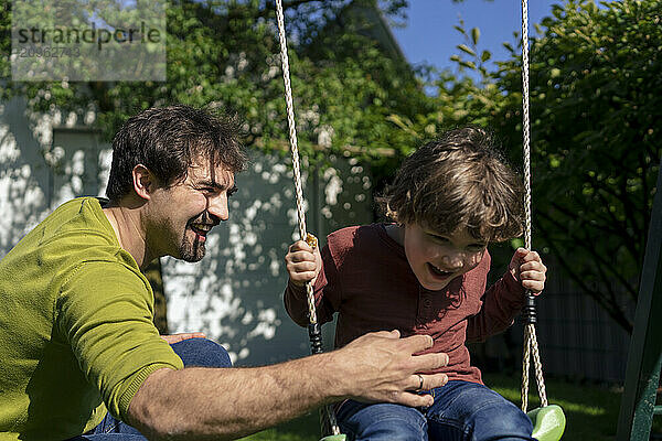 Happy father with son swinging in back yard