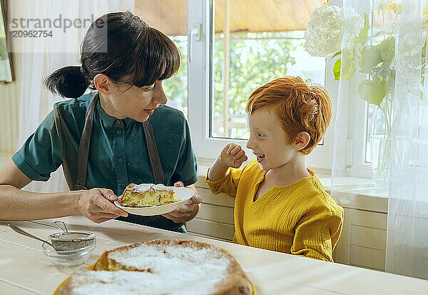 Mother serving slice of apple pie to son in kitchen