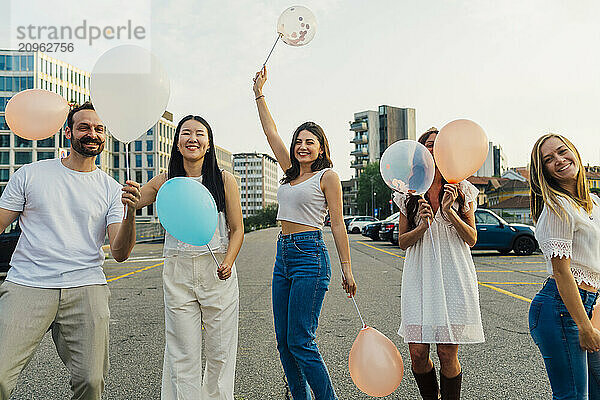 Happy friends holding balloons on road under sky