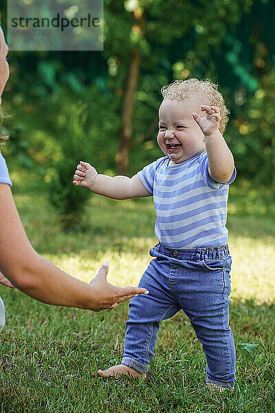 Baby taking first steps outdoors with mother supporting.