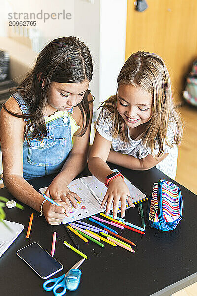 Friends coloring with crayons on book at home