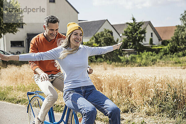 Cheerful man riding bicycle with woman in front of houses