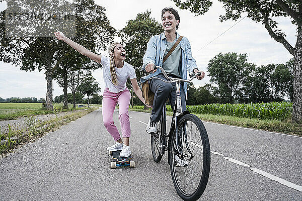 Carefree woman skateboarding with boyfriend riding bicycle on road