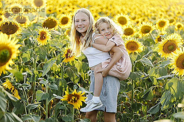 Girl piggybacking sister in sunflower field