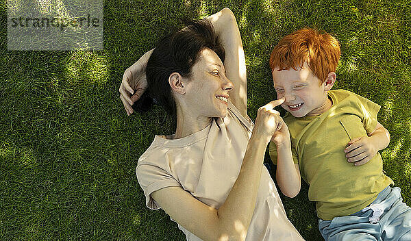 Joyful mother lying on grass and spending leisure time with son in garden