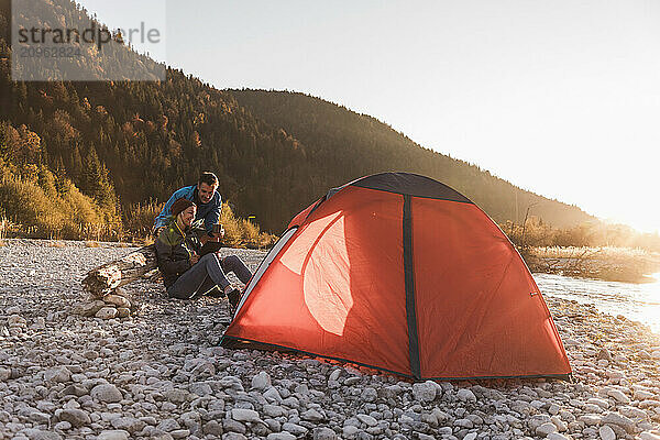 Mature couple sitting near tent at riverside