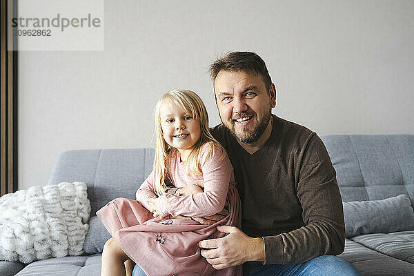 Happy daughter sitting on lap of father at home