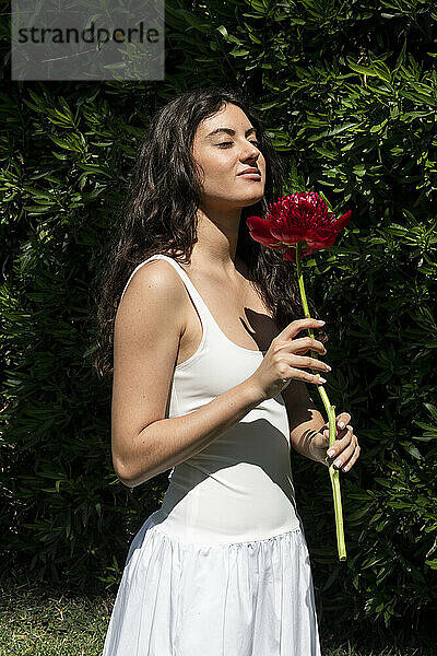 Beautiful woman with eyes closed smelling flower near plants