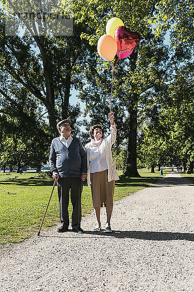 Happy senior man with woman holding balloons in park