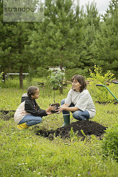 Grandchild planting apple tree with grandmother in garden