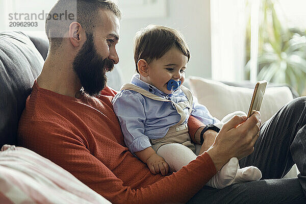 Father with son watching cartoons on smart phone at home