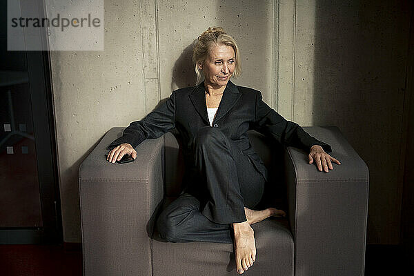 Senior businesswoman sitting on armchair near wall