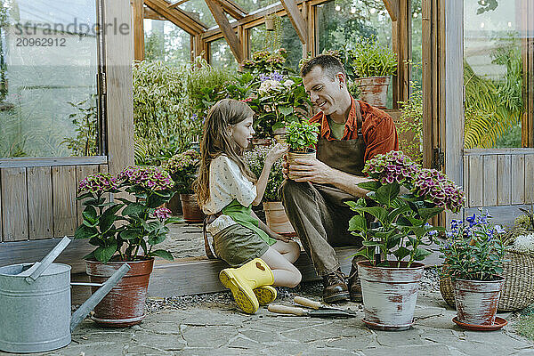 Girl spending leisure time with father holding potted plant near greenhouse