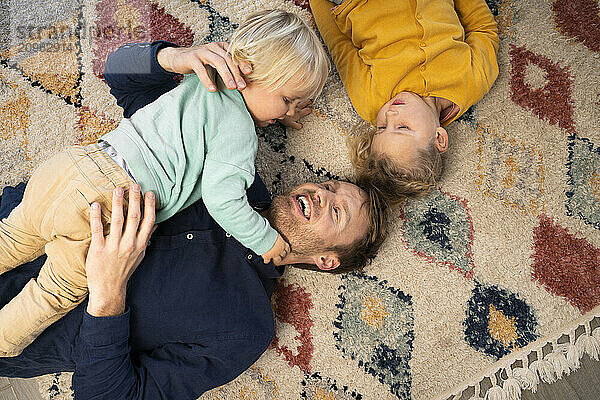 Smiling father lying down with son and daughter on carpet at home