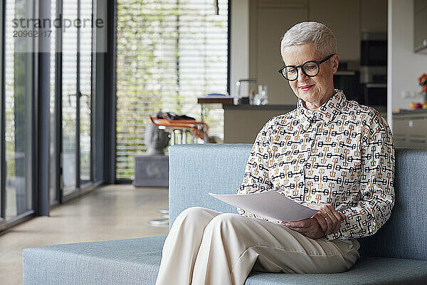 Senior woman sitting on couch at home reading document