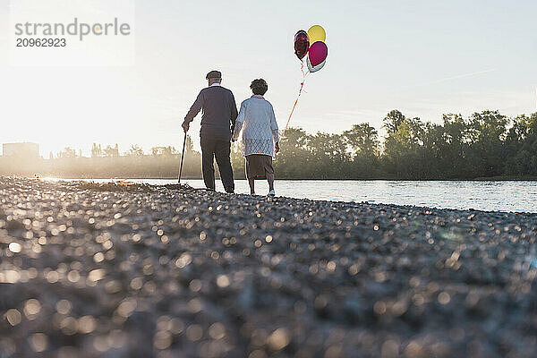 Senior couple holding balloon and walking near river