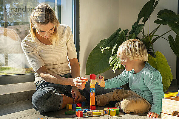 Happy son playing building blocks with mother sitting at home