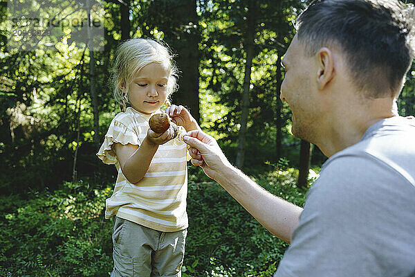 Girl holding Boletus mushroom standing with father in forest