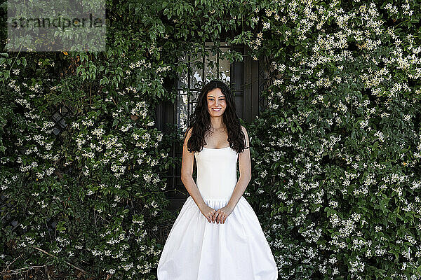 Smiling woman with hand clasped standing near plants