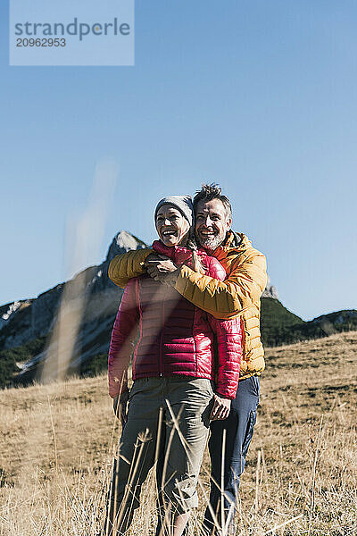 Happy man embracing friend standing on mountain under blue sky